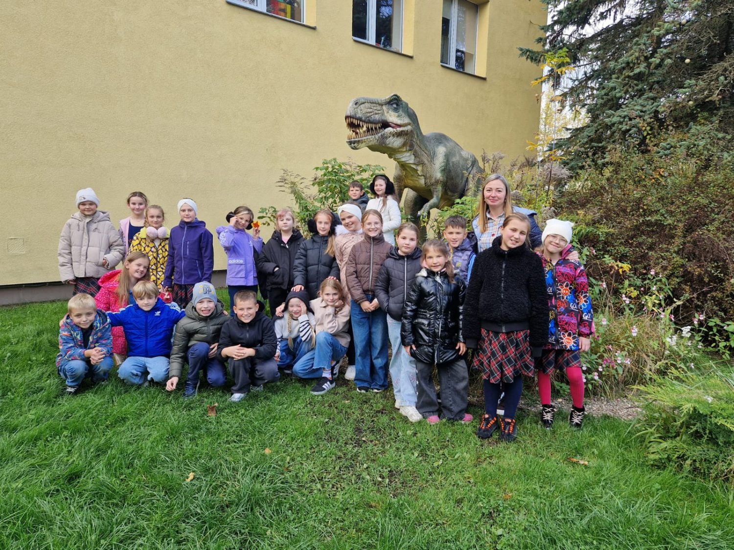 3.b klase zoodarzā pie dinozaura stajuas kopbilde ar audzinātāju